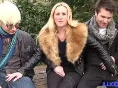 Blonde in offenem Mantel spreizt die Beine weit auf einem alten Picknicktisch im Park