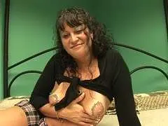 Reife schwarzhaarige Hausfrau im tiefen Ausschnitt auf dem Bett