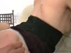 Schlanke Schwarzhaarige mit frechem Kurzhaarschnitt sitzt lächelnd in schwarzem Corsage-Top und Strümpfen auf hellem Sofa