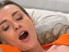 Schwarzhaarige im engen orangen Top mit tiefem Ausschnitt sitzt neben überraschtem Mann auf hellem Wohnzimmersofa