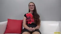 Schüchternes Brillenmädchen mit langem braunem Haar und roter Blume auf weißer Couch sitzend